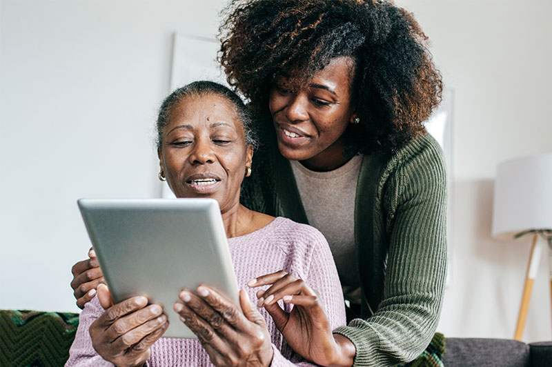 A woman helping an older adult use a tablet