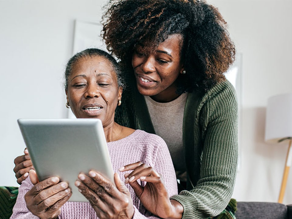 A caregiver helping an older woman use a tablet